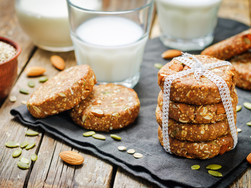 Quinoa Energieriegel mit Datteln und Mandelmus, rund geformt und gestapelt, liegen auf einem Tisch, im Hintergrund ist ein Glas Milch und Nüsse dienen als Dekoration